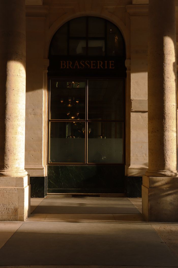 A sunlit entrance to a Parisian brasserie showcasing classical architecture.
