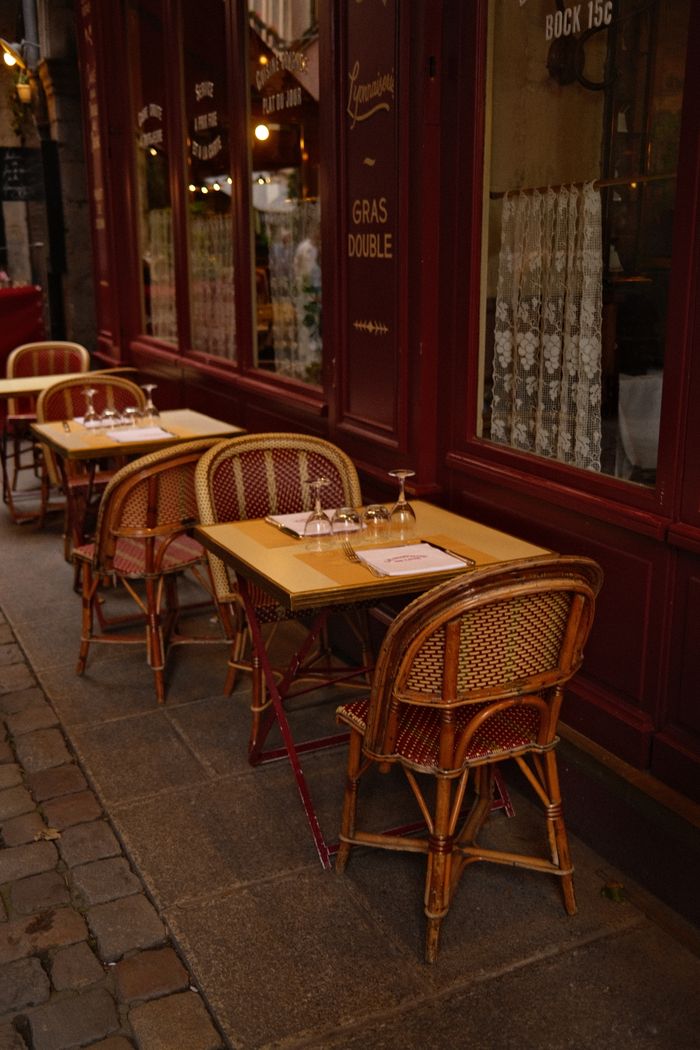 A cozy outdoor seating area at a Parisian cafe with wicker chairs and tables on a cobblestone sidewalk.
