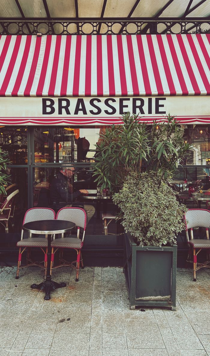 Cozy outdoor seating at a Parisian brasserie under a vibrant striped awning, embodying classic European café culture.